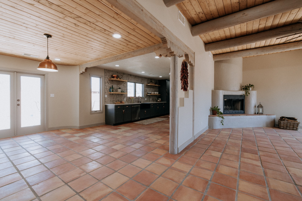 Idée de décoration pour un grand salon sud-ouest américain ouvert avec un mur beige, tomettes au sol, une cheminée d'angle, un manteau de cheminée en plâtre et un sol orange.