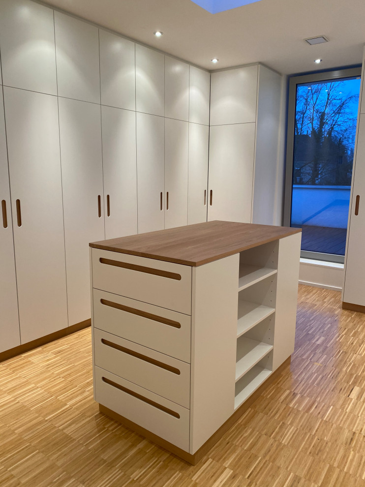 Geräumiges, Neutrales Modernes Ankleidezimmer mit Ankleidebereich, flächenbündigen Schrankfronten, weißen Schränken, hellem Holzboden und braunem Boden in Sonstige