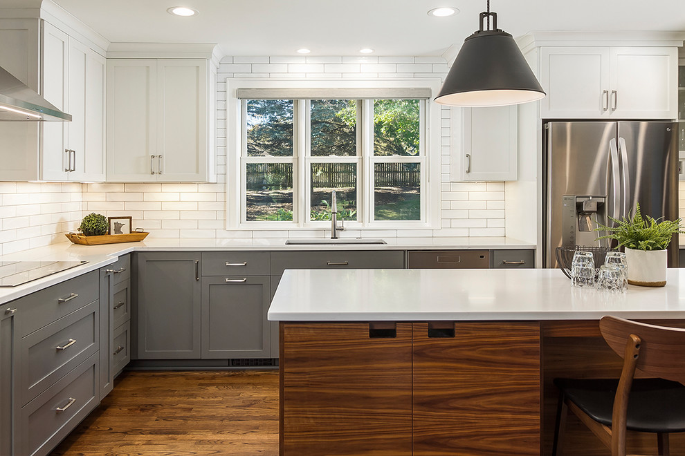 Mid-sized transitional l-shaped eat-in kitchen in Minneapolis with an undermount sink, shaker cabinets, grey cabinets, quartzite benchtops, white splashback, subway tile splashback, stainless steel appliances, medium hardwood floors, with island, brown floor and white benchtop.
