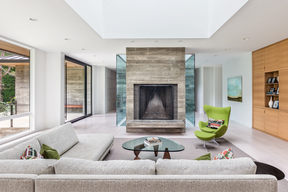 Large contemporary open concept living room in Charleston with white walls, a standard fireplace, a concrete fireplace surround and light hardwood floors.