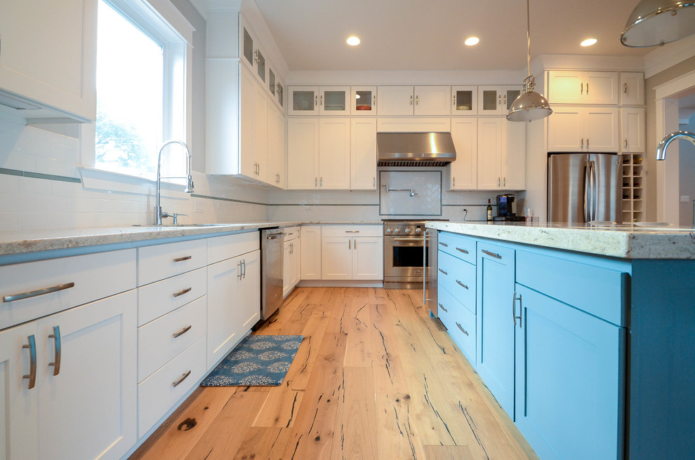 Photo of a mid-sized traditional l-shaped open plan kitchen in New Orleans with an undermount sink, flat-panel cabinets, white cabinets, granite benchtops, white splashback, ceramic splashback, stainless steel appliances, light hardwood floors and with island.