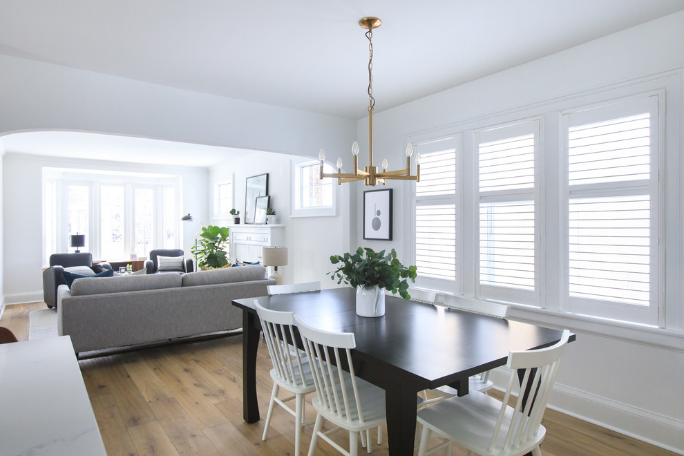 Inspiration for a mid-sized transitional open plan dining in Toronto with white walls, light hardwood floors, a standard fireplace, a wood fireplace surround and brown floor.