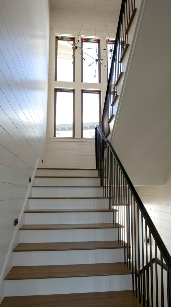 На фото: большая п-образная лестница в морском стиле с деревянными ступенями, металлическими перилами, крашенными деревянными подступенками и стенами из вагонки