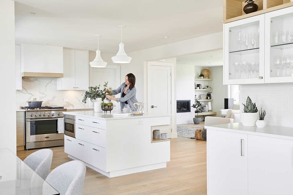 Mid-sized scandinavian l-shaped eat-in kitchen in Vancouver with an undermount sink, flat-panel cabinets, white cabinets, quartzite benchtops, white splashback, ceramic splashback, stainless steel appliances, light hardwood floors, with island, brown floor and white benchtop.