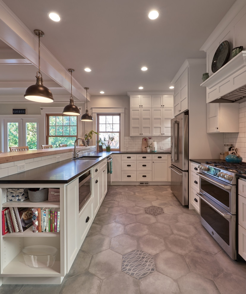 This is an example of a mid-sized country u-shaped eat-in kitchen in Seattle with a double-bowl sink, shaker cabinets, white cabinets, granite benchtops, white splashback, subway tile splashback, stainless steel appliances, porcelain floors, a peninsula, grey floor and black benchtop.