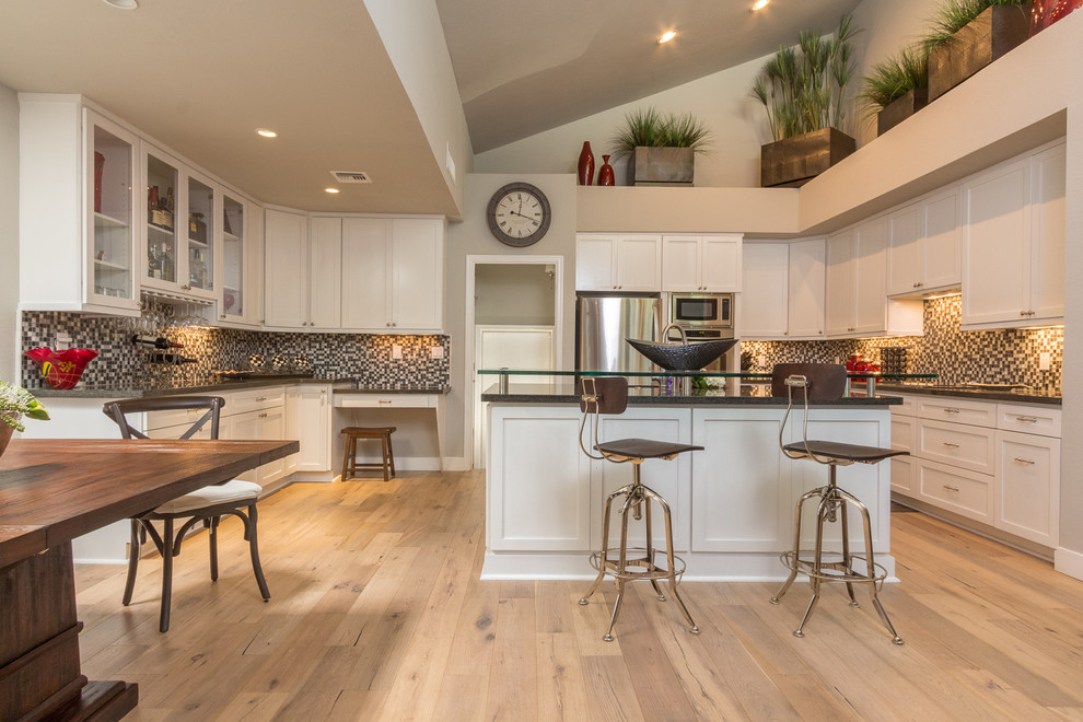 Photo of an expansive country u-shaped open plan kitchen in Phoenix with a farmhouse sink, shaker cabinets, white cabinets, granite benchtops, white splashback, glass tile splashback, stainless steel appliances, light hardwood floors and with island.