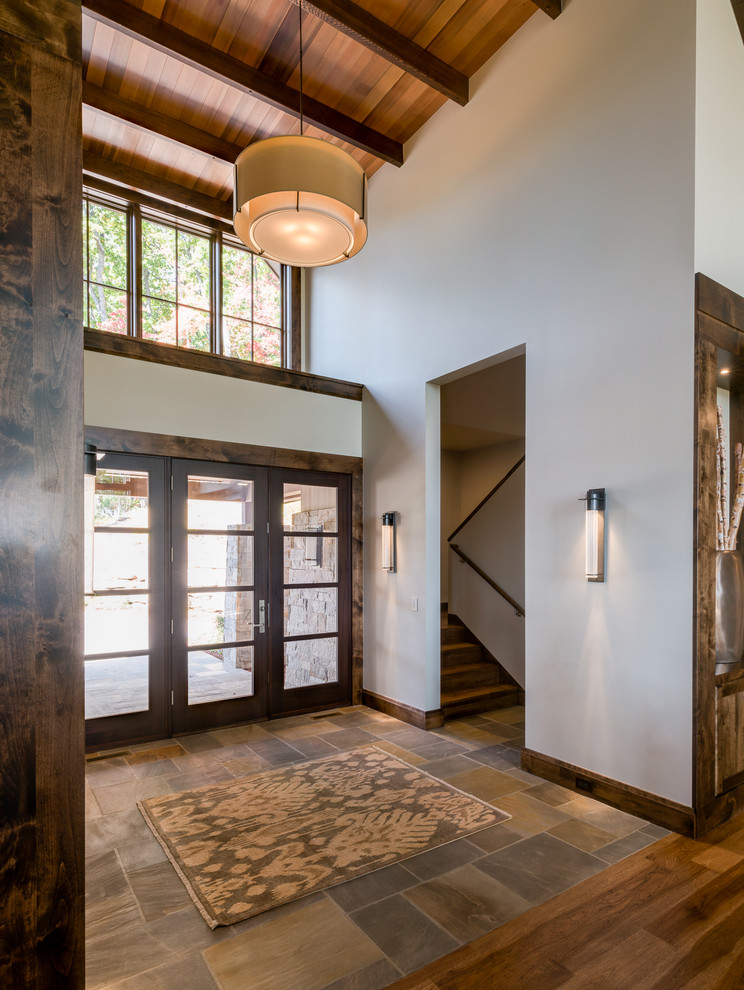 Example of a large mountain style slate floor single front door design with beige walls and a glass front door