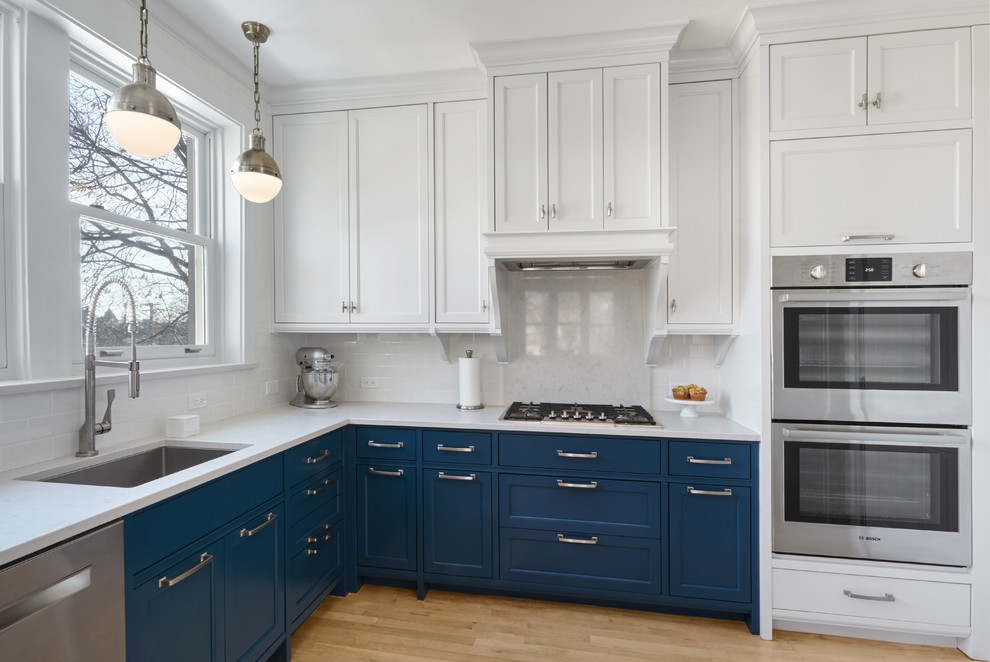 Inspiration for a traditional l-shaped kitchen in Chicago with an undermount sink, shaker cabinets, blue cabinets, white splashback, stainless steel appliances and light hardwood floors.