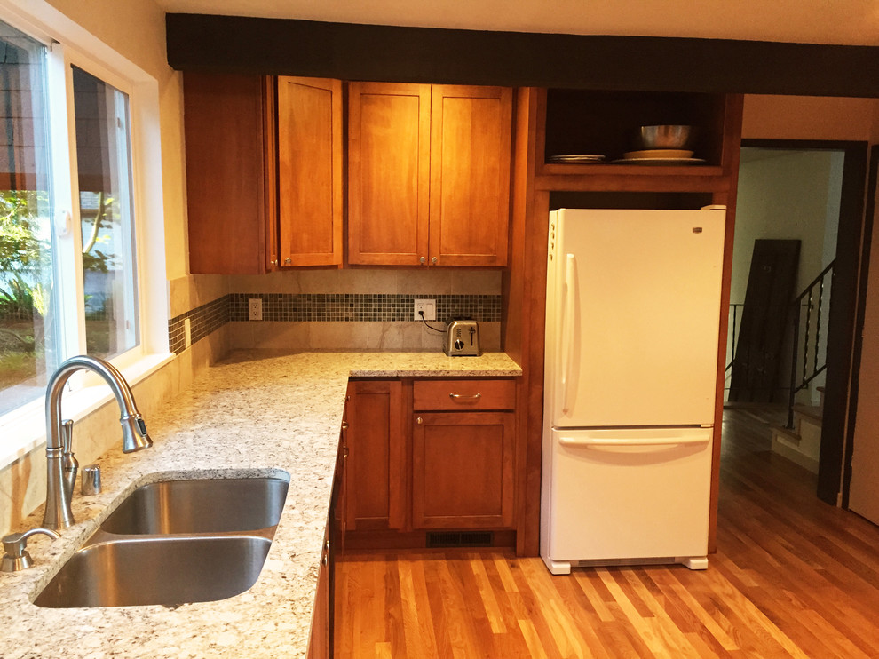 Photo of a mid-sized contemporary u-shaped eat-in kitchen in Seattle with an undermount sink, shaker cabinets, medium wood cabinets, solid surface benchtops, beige splashback, porcelain splashback, black appliances, medium hardwood floors and no island.