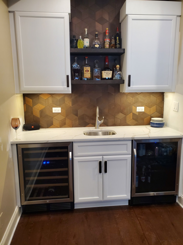 This is an example of a small transitional single-wall wet bar in Chicago with an undermount sink, recessed-panel cabinets, white cabinets, quartz benchtops, multi-coloured splashback, ceramic splashback, medium hardwood floors, brown floor and white benchtop.