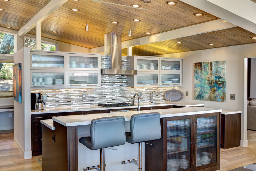 This is an example of a large contemporary u-shaped open plan kitchen in Sacramento with glass-front cabinets, dark wood cabinets, matchstick tile splashback, stainless steel appliances, light hardwood floors, with island, an undermount sink, quartz benchtops and grey splashback.