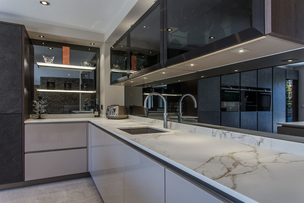 Contemporary l-shaped open plan kitchen in Sussex with flat-panel cabinets, black cabinets, solid surface benchtops, mirror splashback, black appliances and with island.