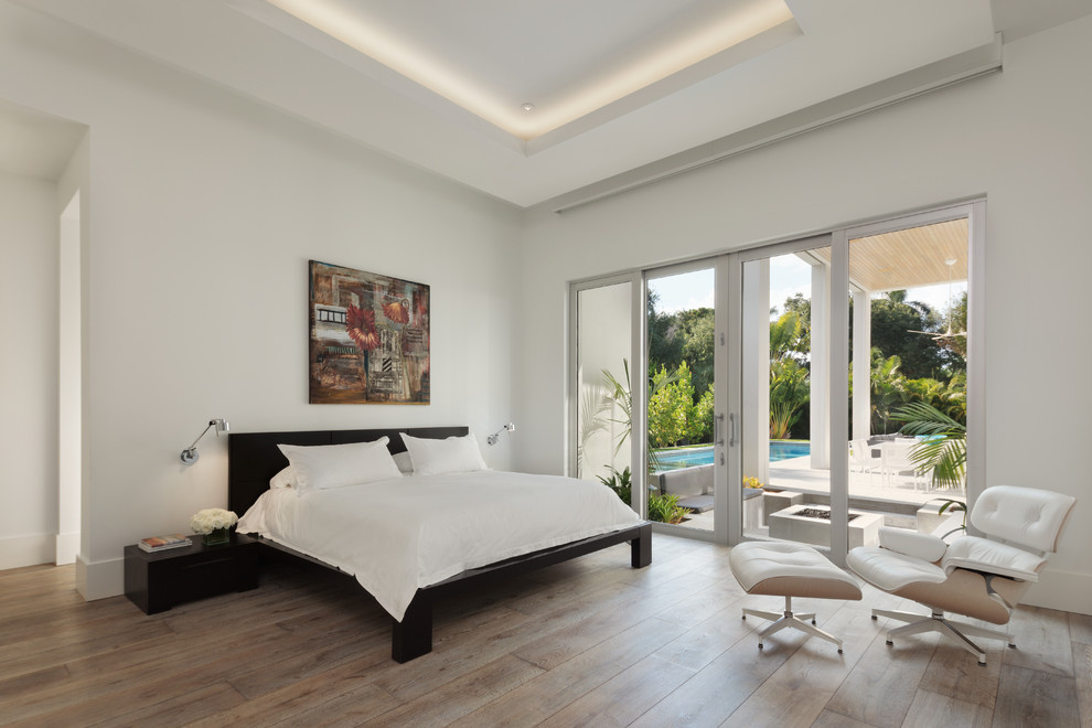 Photo of a contemporary bedroom in Miami with white walls, medium hardwood floors and brown floor.