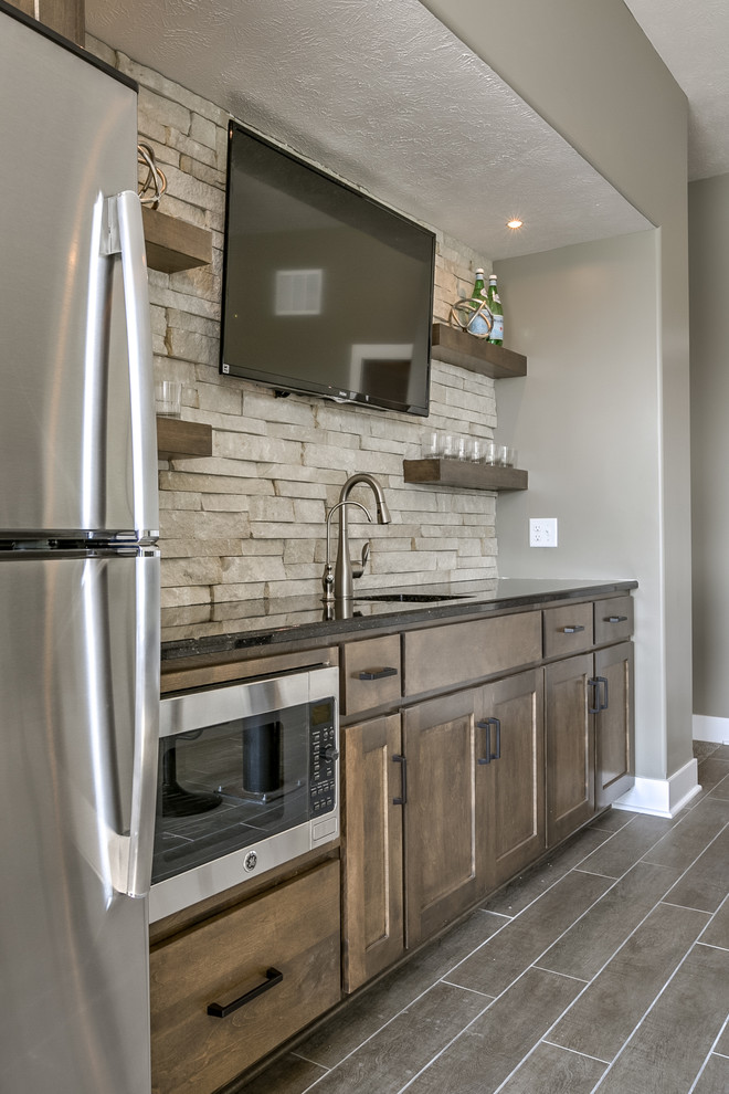 Large traditional single-wall seated home bar in Omaha with an undermount sink, shaker cabinets, dark wood cabinets, beige splashback, stone tile splashback and grey floor.