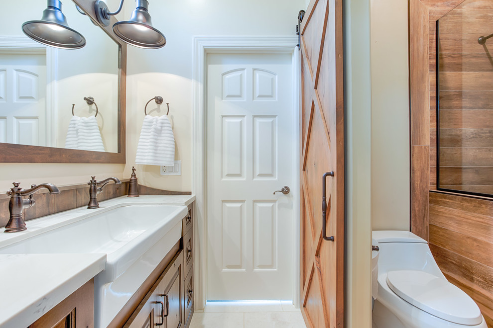 Photo of a mid-sized country 3/4 bathroom in Phoenix with raised-panel cabinets, medium wood cabinets, an alcove tub, an alcove shower, a one-piece toilet, brown tile, porcelain tile, beige walls, marble floors, a trough sink, granite benchtops, white floor and an open shower.