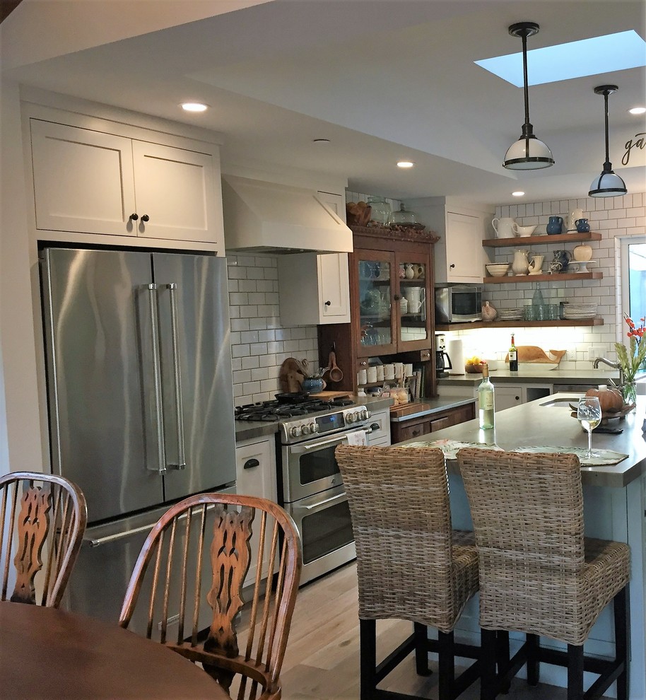 Small beach style l-shaped open plan kitchen in San Diego with a farmhouse sink, shaker cabinets, white cabinets, quartz benchtops, white splashback, ceramic splashback, stainless steel appliances, medium hardwood floors, with island and brown floor.