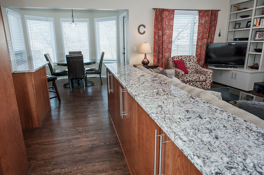Inspiration for a mid-sized transitional enclosed and u-shaped dark wood floor open concept kitchen remodel in Calgary with white walls, a media wall, an undermount sink, flat-panel cabinets, medium tone wood cabinets, granite countertops, white backsplash, mirror backsplash, stainless steel appliances and an island
