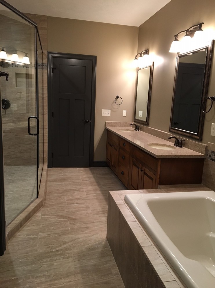 Large transitional master bathroom in Omaha with furniture-like cabinets, medium wood cabinets, a drop-in tub, a corner shower, beige tile, porcelain tile, beige walls, porcelain floors, an undermount sink, granite benchtops, beige floor and a hinged shower door.