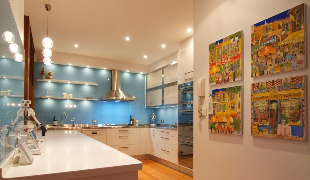 Design ideas for a mid-sized modern l-shaped separate kitchen in Sydney with an integrated sink, flat-panel cabinets, white cabinets, stainless steel benchtops, blue splashback, glass sheet splashback, stainless steel appliances, light hardwood floors, with island and white benchtop.