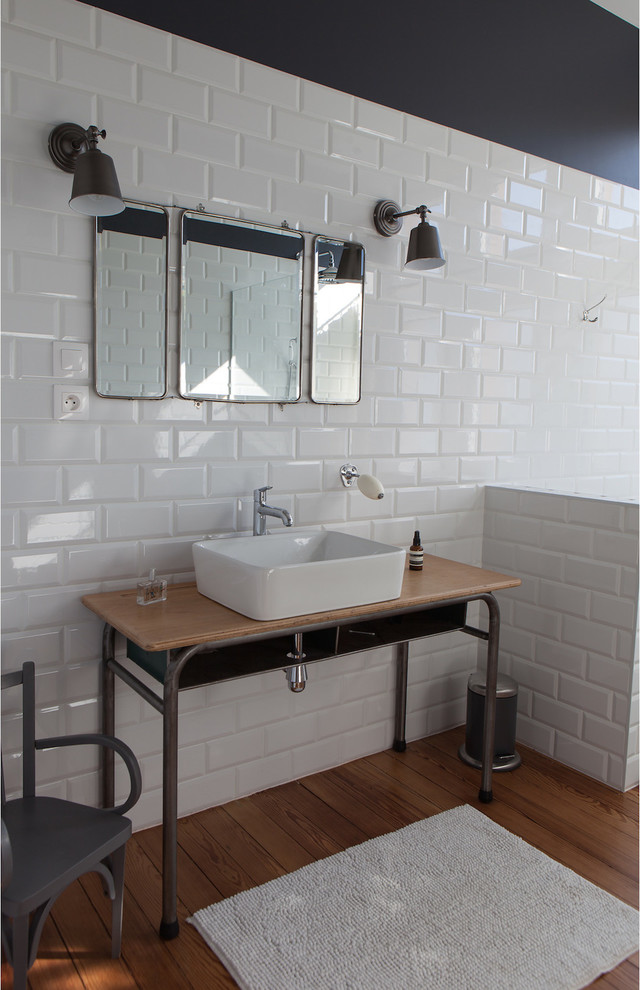 Mid-sized industrial master bathroom in Nancy with a vessel sink, wood benchtops, white tile, subway tile, black walls, medium hardwood floors and brown benchtops.