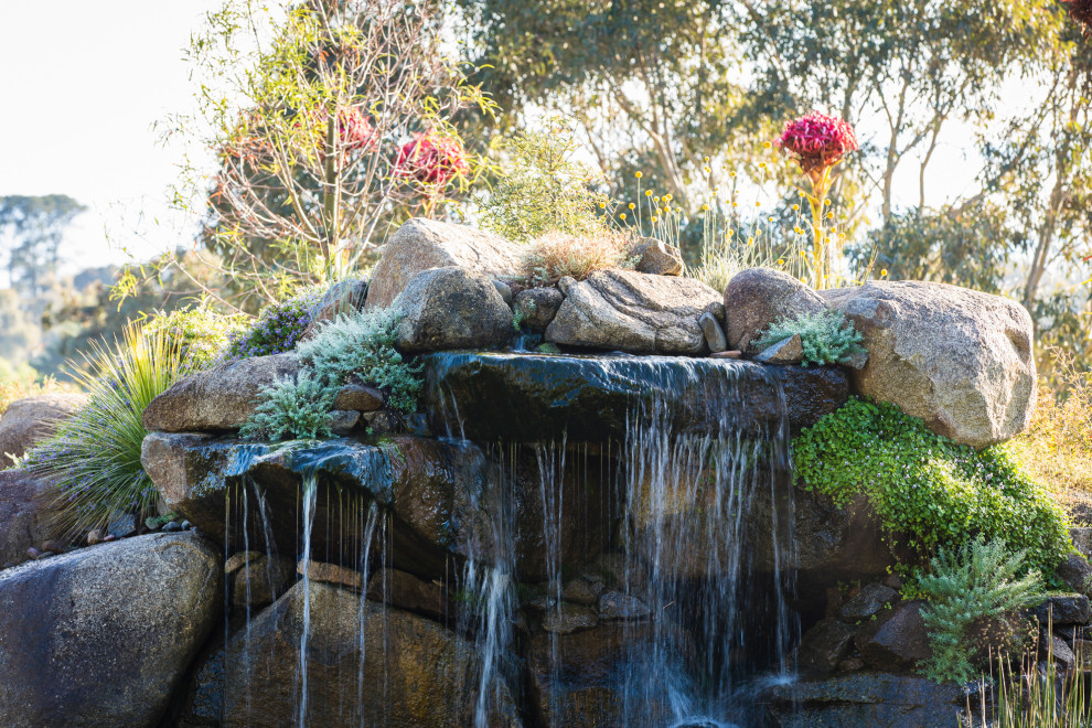 Large sloped full sun formal garden in Melbourne with with pond and gravel for spring.