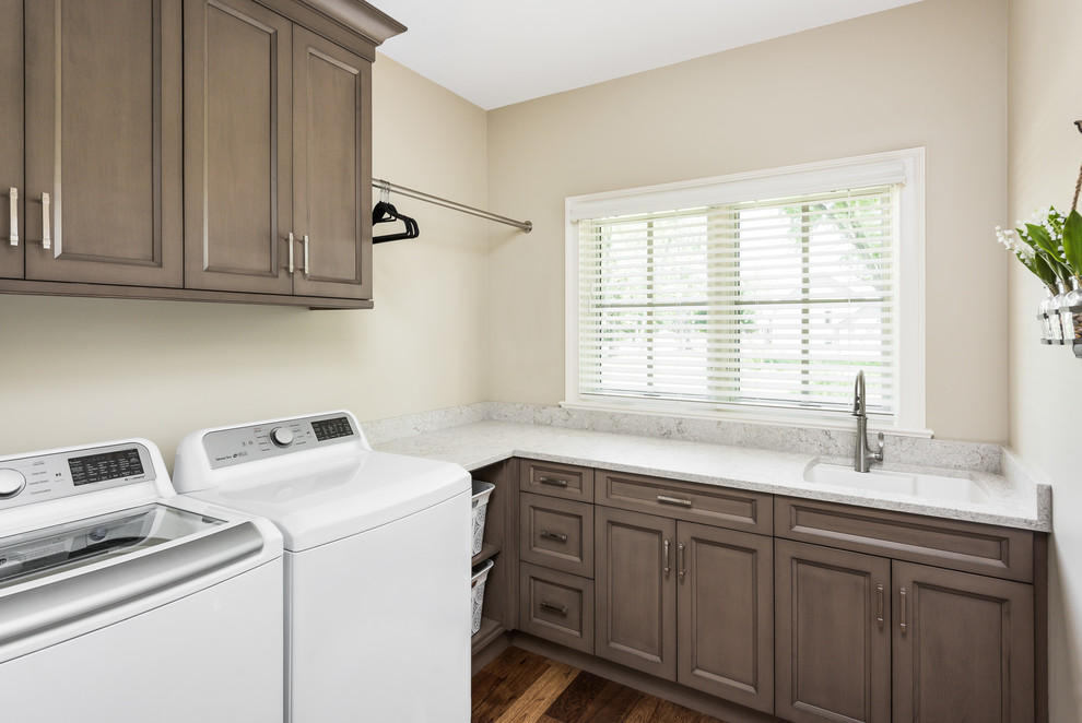 Mid-sized traditional l-shaped dedicated laundry room in Chicago with an undermount sink, recessed-panel cabinets, brown cabinets, quartz benchtops, beige walls, dark hardwood floors, a side-by-side washer and dryer, brown floor and white benchtop.