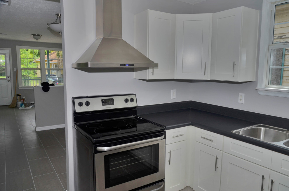 Inspiration for a mid-sized u-shaped porcelain tile and beige floor eat-in kitchen remodel with a drop-in sink, shaker cabinets, white cabinets, laminate countertops, stainless steel appliances, no island and black countertops