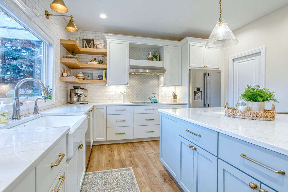Example of a large transitional l-shaped beige floor kitchen design with a farmhouse sink, flat-panel cabinets, white cabinets, beige backsplash, ceramic backsplash, stainless steel appliances, an island and white countertops