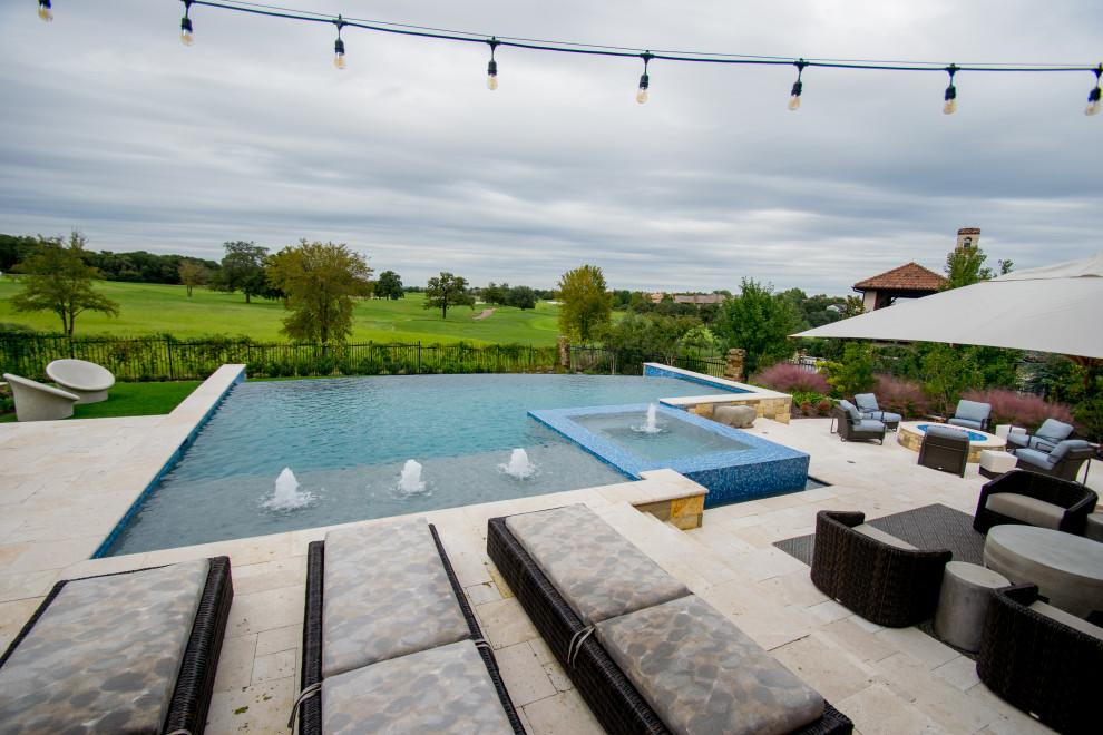 Photo of a large transitional backyard custom-shaped infinity pool in Dallas with a water feature and natural stone pavers.