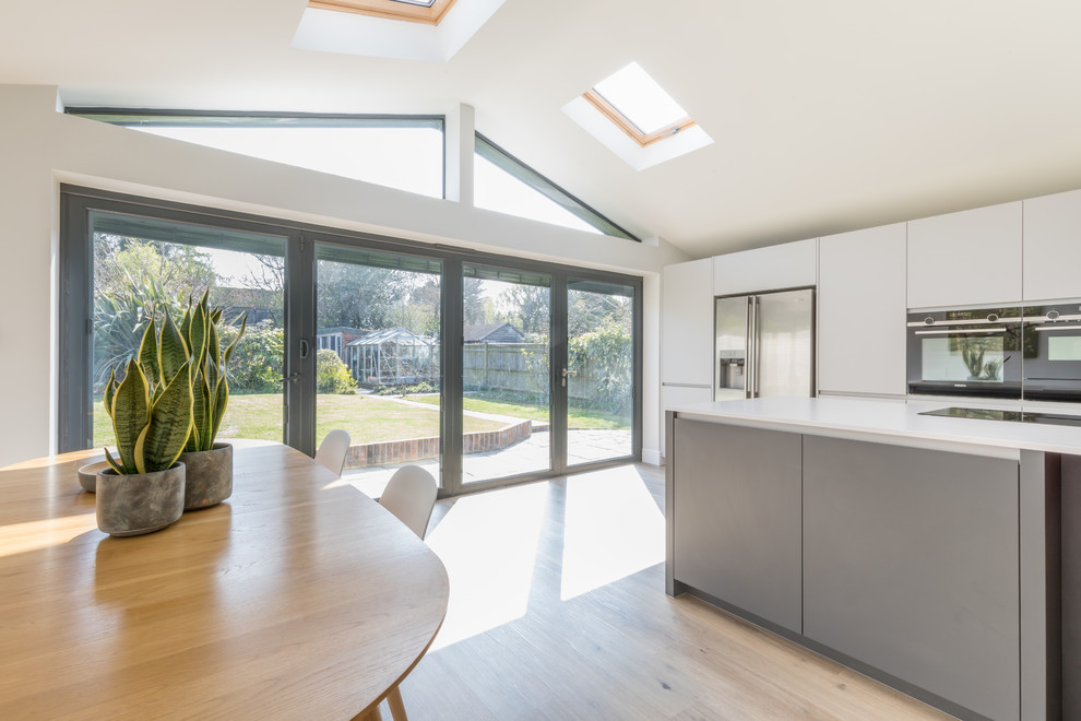 Mid-sized contemporary galley open plan kitchen in Sussex with an integrated sink, flat-panel cabinets, grey cabinets, solid surface benchtops, stainless steel appliances, with island and white benchtop.
