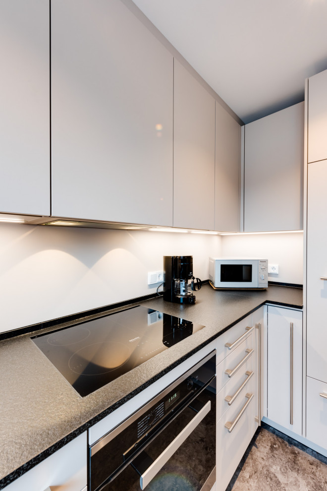 Inspiration for a mid-sized contemporary l-shaped separate kitchen in Hamburg with a single-bowl sink, flat-panel cabinets, white cabinets, laminate benchtops, white splashback, glass sheet splashback, black appliances, linoleum floors, a peninsula, grey floor, black benchtop and coffered.