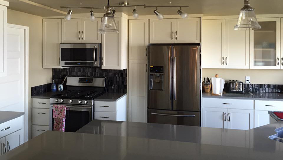 Example of a mid-sized transitional l-shaped open concept kitchen design in Seattle with an undermount sink, shaker cabinets, white cabinets, quartzite countertops, metallic backsplash, glass tile backsplash, stainless steel appliances and an island