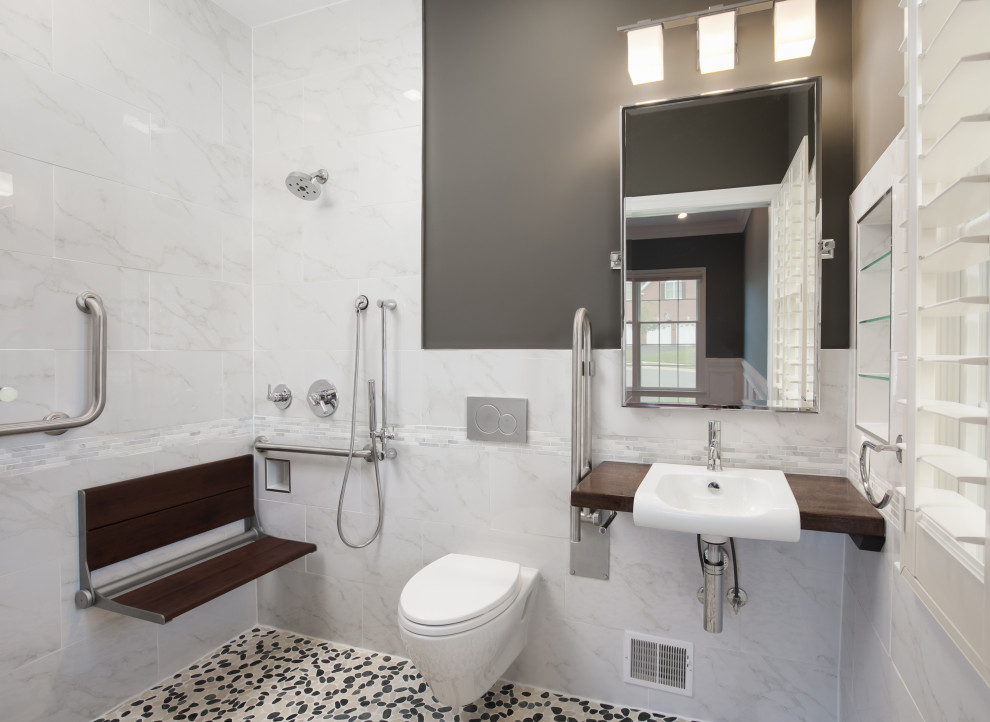 Photo of a small transitional master bathroom in DC Metro with medium wood cabinets, a curbless shower, a wall-mount toilet, multi-coloured tile, porcelain tile, grey walls, pebble tile floors, a drop-in sink, wood benchtops, multi-coloured floor, blue benchtops, a shower seat, a single vanity, a floating vanity and decorative wall panelling.