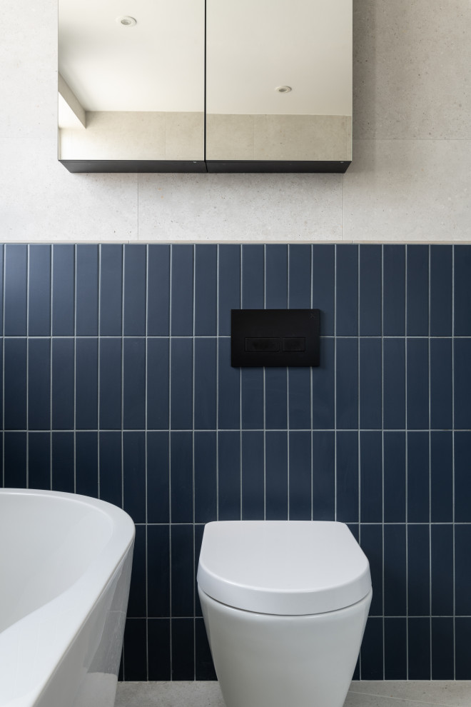 This is an example of a mid-sized contemporary kids bathroom in London with a freestanding tub, an open shower, a one-piece toilet, gray tile, porcelain tile, grey walls, porcelain floors, a wall-mount sink, concrete benchtops, grey floor, a hinged shower door, orange benchtops and a single vanity.