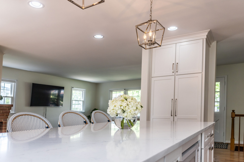 Example of a mid-sized transitional l-shaped light wood floor and brown floor eat-in kitchen design in Baltimore with an undermount sink, shaker cabinets, white cabinets, quartz countertops, white backsplash, marble backsplash, stainless steel appliances, an island and white countertops