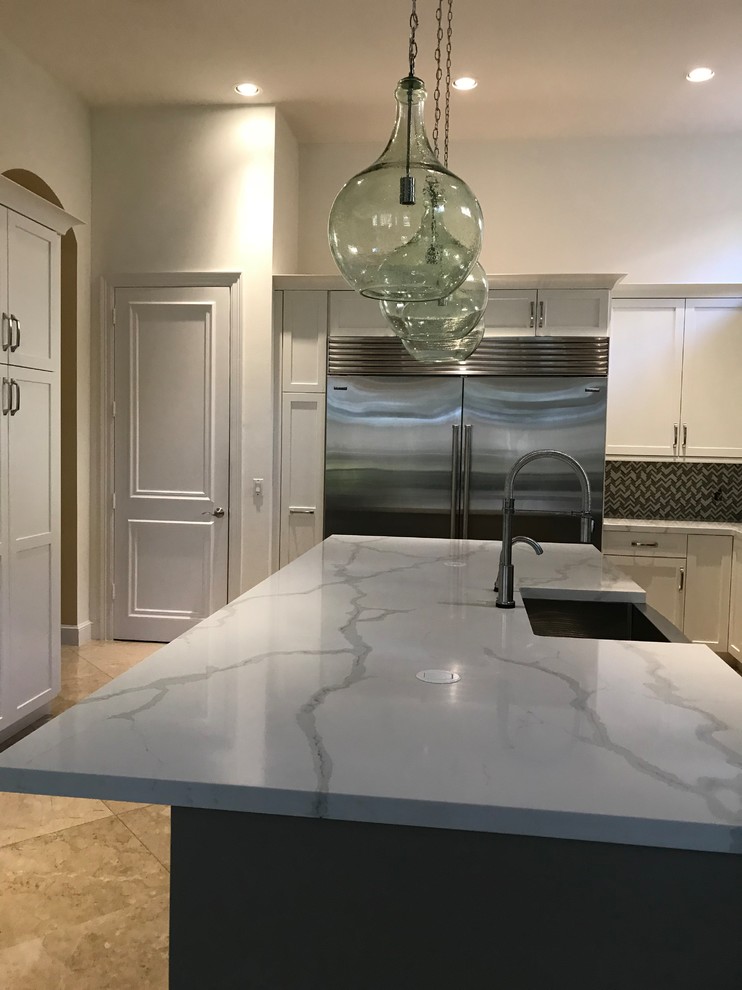 Kitchen - large transitional kitchen idea in Miami with a farmhouse sink, shaker cabinets, white cabinets, quartz countertops, gray backsplash, glass tile backsplash, stainless steel appliances, an island and multicolored countertops