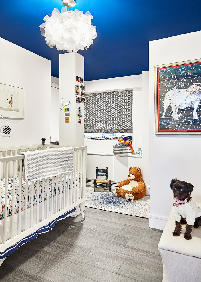 Photo of a small contemporary nursery for boys in New York with white walls, light hardwood floors and grey floor.