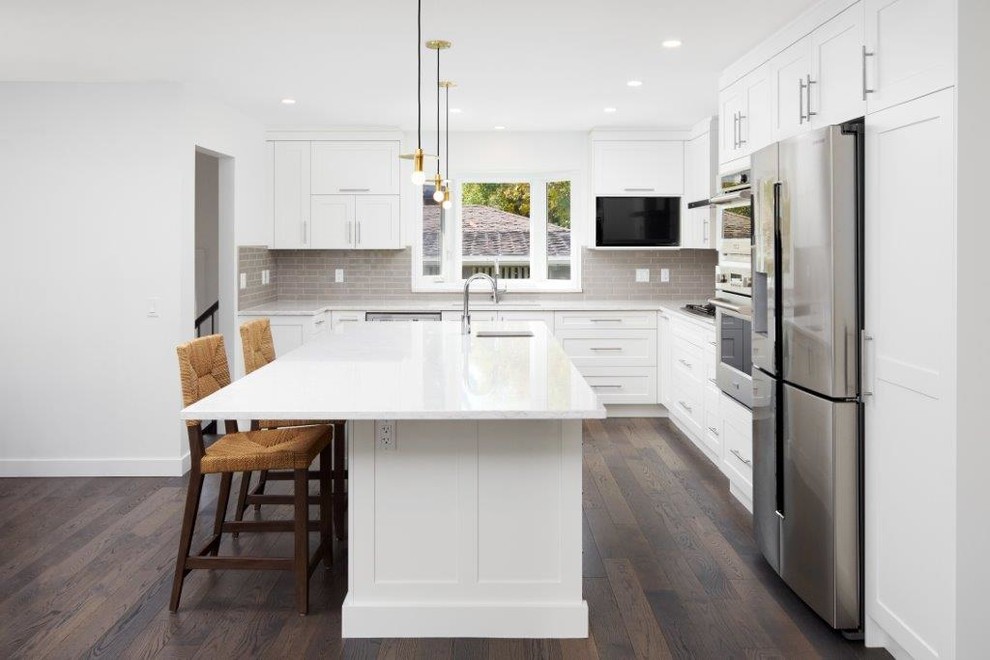Inspiration for a mid-sized transitional l-shaped dark wood floor and brown floor open concept kitchen remodel in Calgary with an undermount sink, shaker cabinets, white cabinets, quartz countertops, gray backsplash, subway tile backsplash, stainless steel appliances and an island