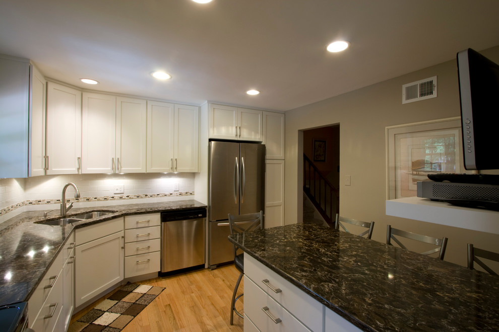 Example of a large transitional l-shaped light wood floor enclosed kitchen design in DC Metro with an undermount sink, shaker cabinets, white cabinets, granite countertops, white backsplash, subway tile backsplash, stainless steel appliances and an island