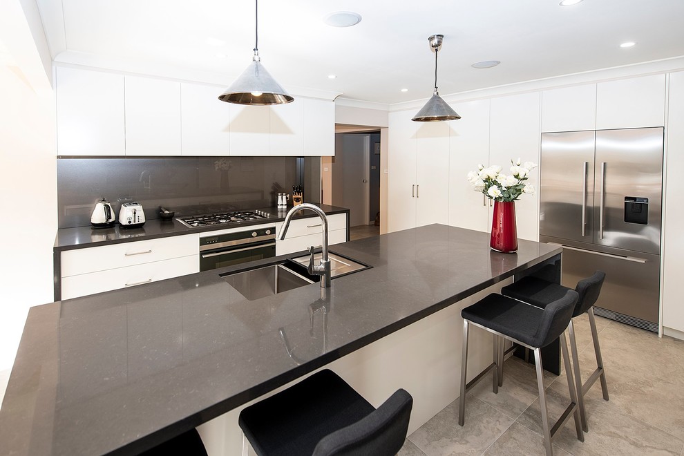 This is an example of a large contemporary open plan kitchen in Sydney with an undermount sink, flat-panel cabinets, white cabinets, quartz benchtops, metallic splashback, glass sheet splashback, stainless steel appliances, porcelain floors, with island, grey floor and grey benchtop.