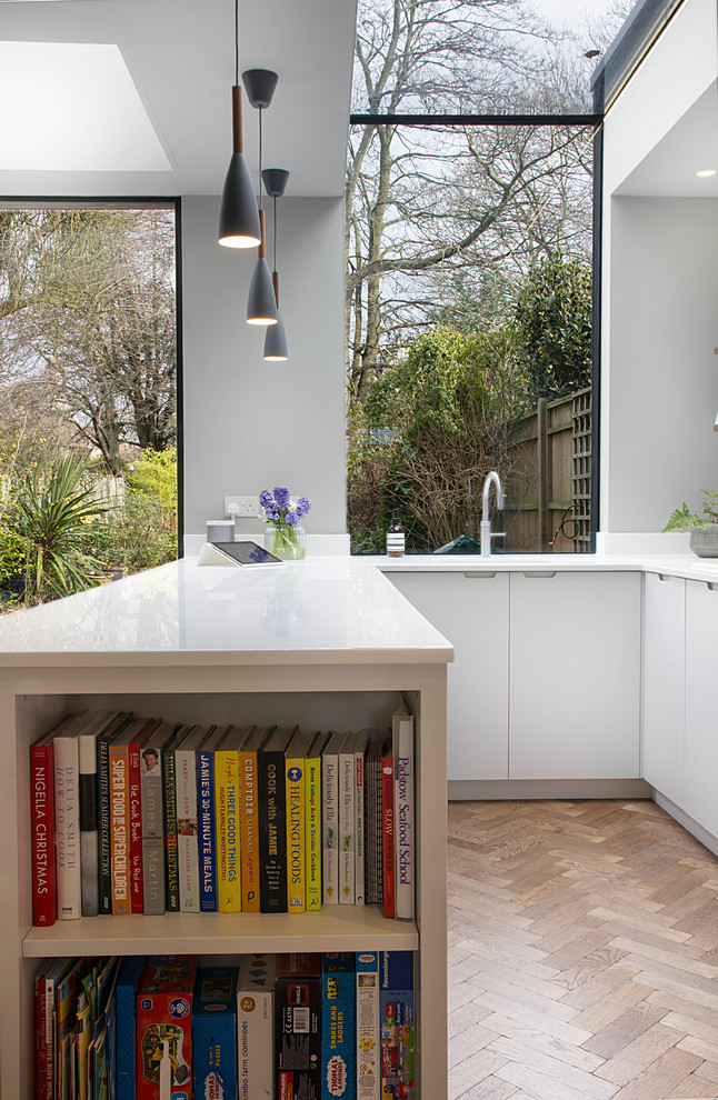 Design ideas for a mid-sized contemporary u-shaped open plan kitchen in London with a single-bowl sink, flat-panel cabinets, white cabinets, solid surface benchtops, metallic splashback, stainless steel appliances, a peninsula and brown floor.