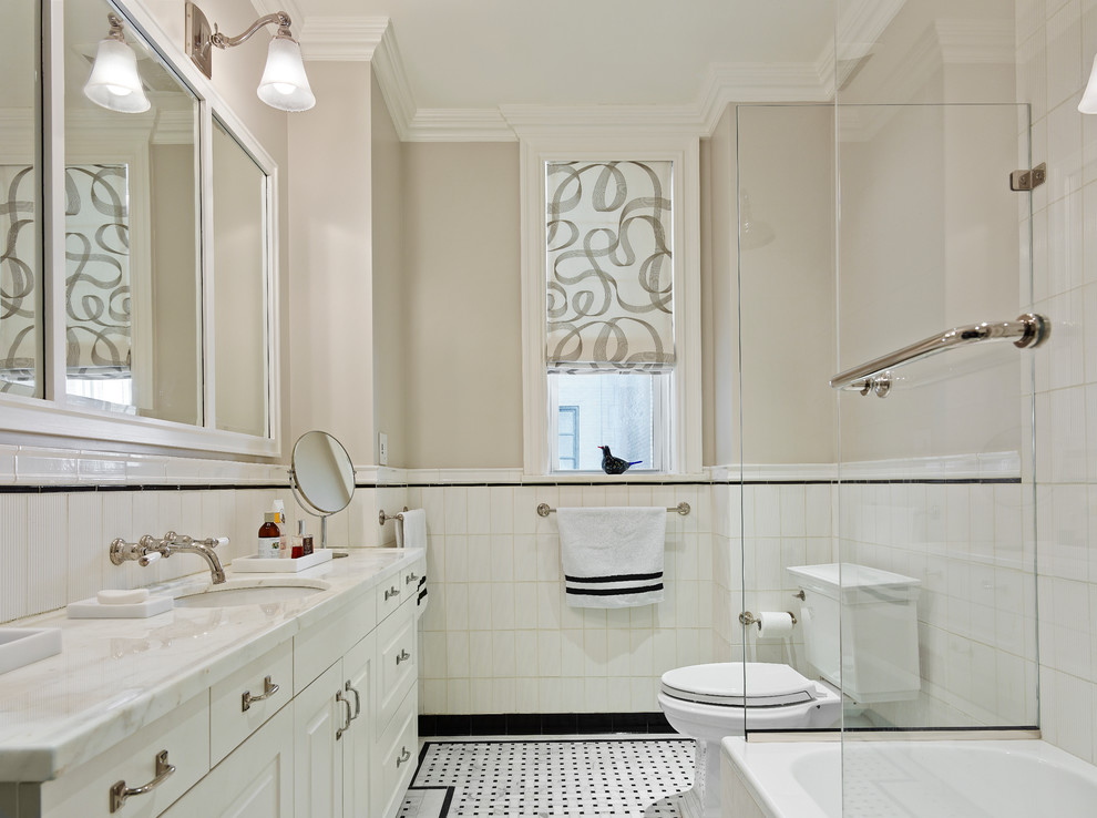 This is an example of a mid-sized contemporary bathroom in New York with an undermount sink, shaker cabinets, white cabinets, marble benchtops, a corner tub, a shower/bathtub combo, a two-piece toilet, black and white tile, ceramic tile, beige walls and ceramic floors.