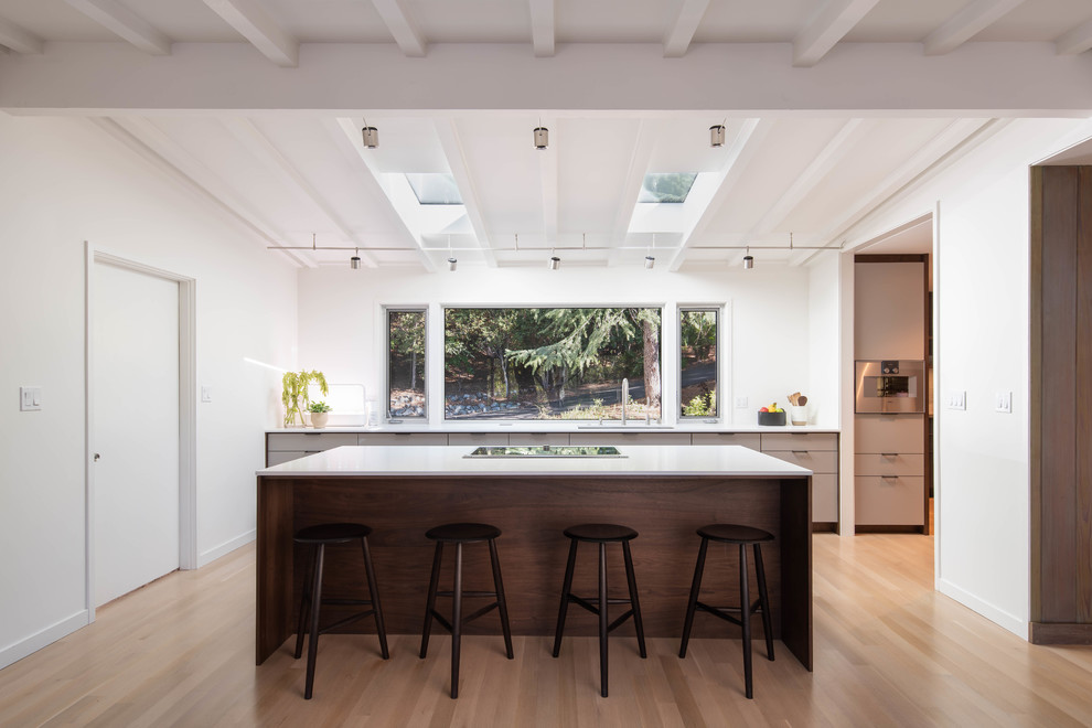 Photo of a midcentury galley kitchen in San Francisco with an undermount sink, flat-panel cabinets, grey cabinets, stainless steel appliances, light hardwood floors, with island, beige floor and white benchtop.