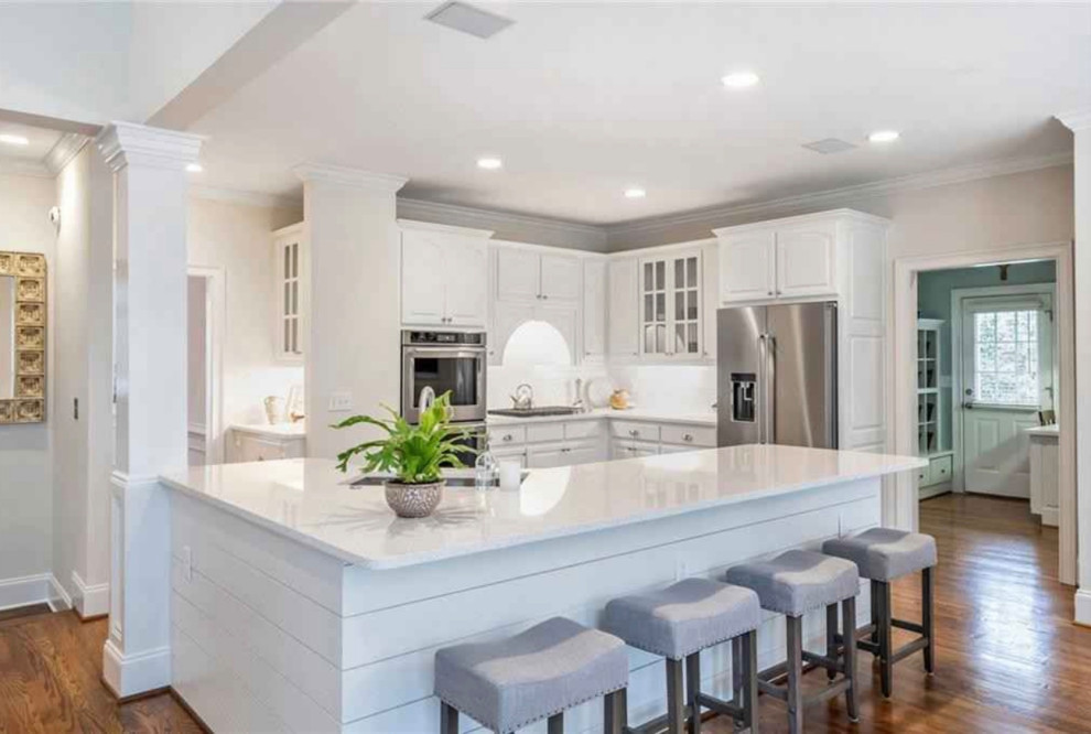 Inspiration for a mid-sized transitional l-shaped kitchen in Atlanta with raised-panel cabinets, white cabinets, quartzite benchtops, white splashback, ceramic splashback, stainless steel appliances, dark hardwood floors, with island and white benchtop.