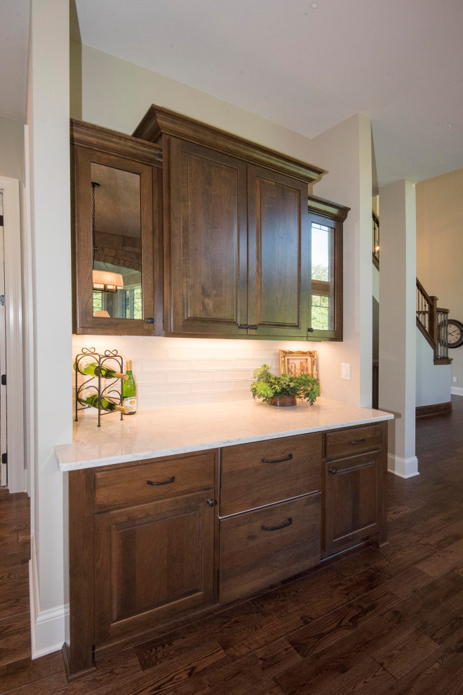 This is an example of a large transitional u-shaped eat-in kitchen in Milwaukee with an undermount sink, shaker cabinets, quartz benchtops, white splashback, ceramic splashback, stainless steel appliances, medium hardwood floors, with island, brown floor, white benchtop and brown cabinets.