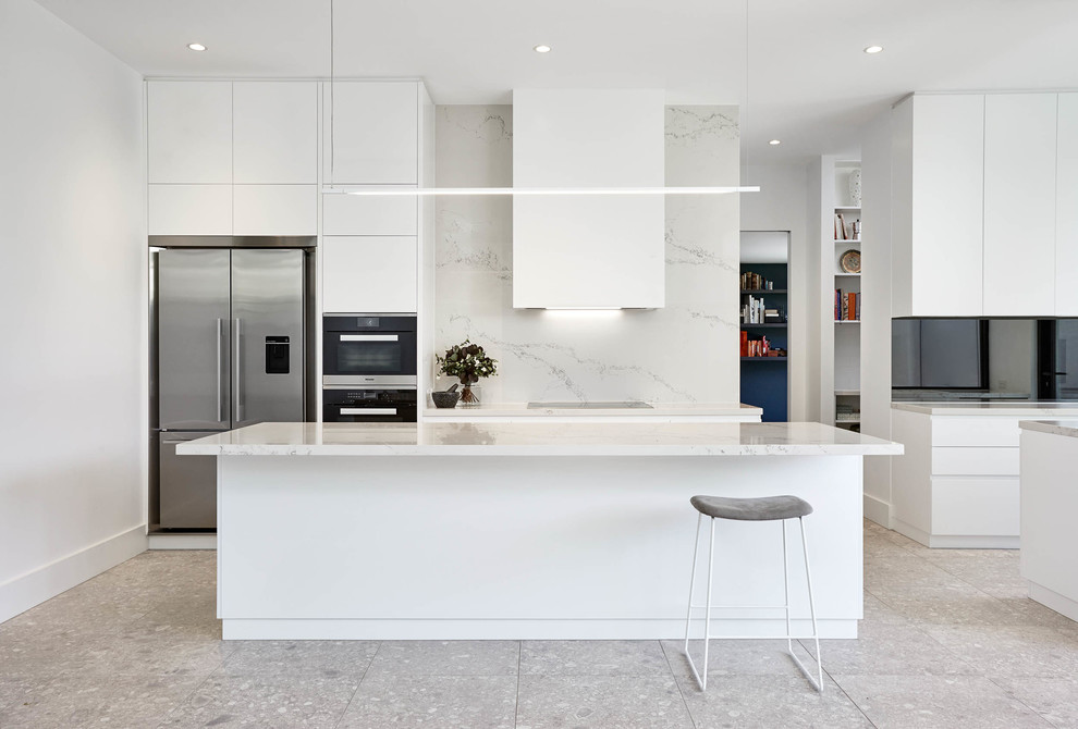 This is an example of a modern galley kitchen in Melbourne with flat-panel cabinets, white cabinets, white splashback, stone slab splashback, stainless steel appliances, with island and grey floor.