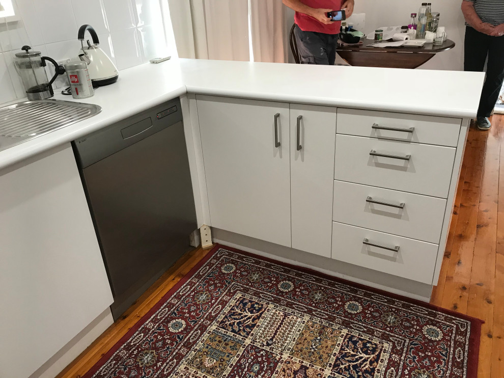 Photo of a contemporary u-shaped kitchen pantry in Sydney with flat-panel cabinets, laminate benchtops, white splashback, a peninsula and white benchtop.