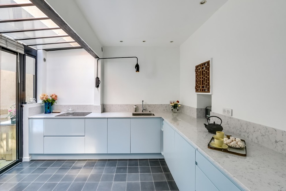 Photo of a large contemporary l-shaped separate kitchen in Paris with an integrated sink, flat-panel cabinets, blue cabinets, quartzite benchtops, white splashback, panelled appliances, cement tiles, grey floor and white benchtop.