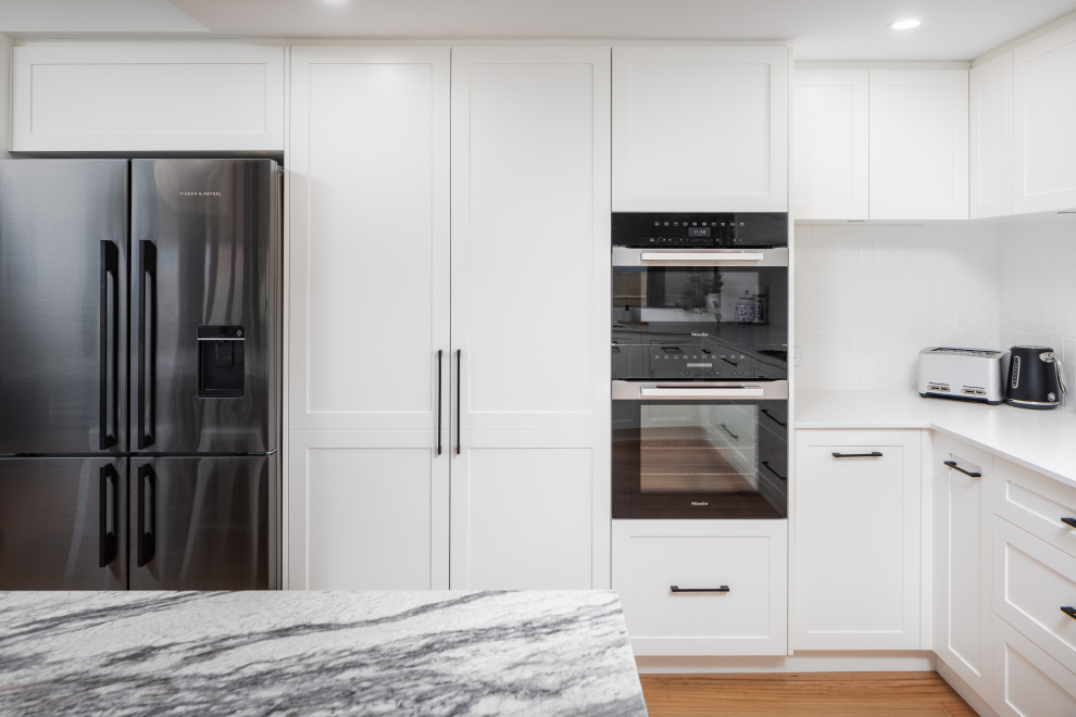 This is an example of a traditional kitchen in Perth with an undermount sink, shaker cabinets, white cabinets, granite benchtops, white splashback, subway tile splashback, black appliances, medium hardwood floors, with island and grey benchtop.