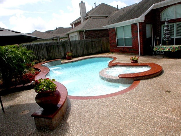 This is an example of a mid-sized traditional backyard custom-shaped pool in Houston with a hot tub and brick pavers.